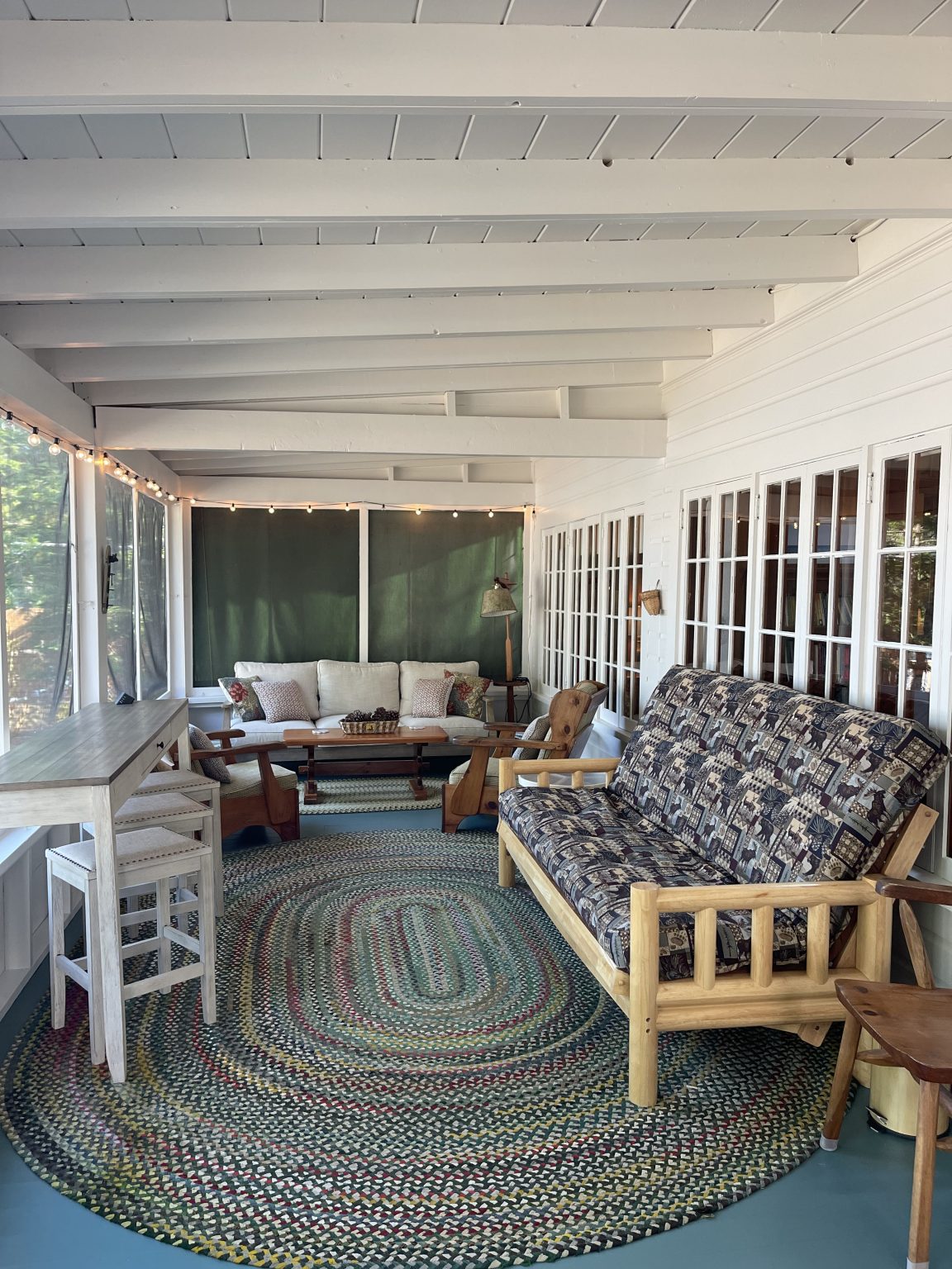 The large screened porch at Sebago Retreat, running the full width of the cottage with wicker seating and lake views