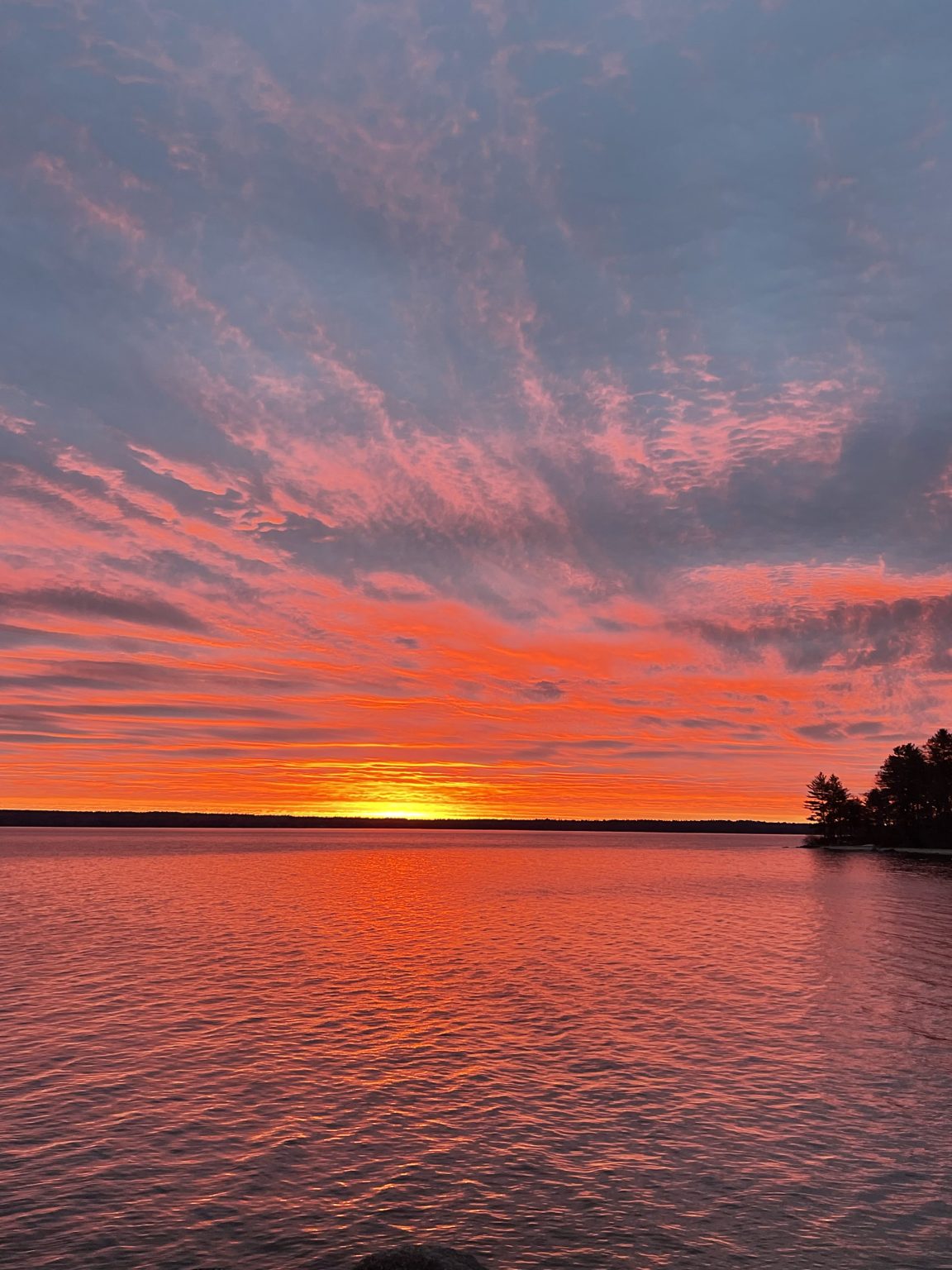 Vivid red sunrise over Sebago Lake seen from the cottage shoreline