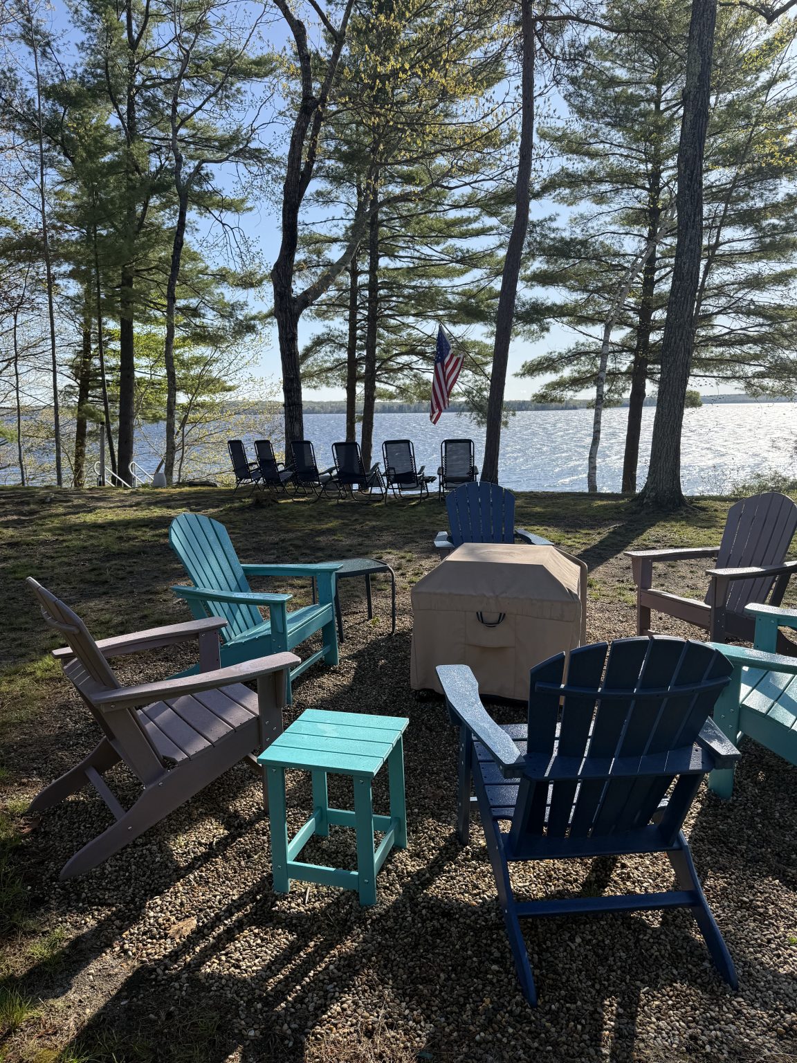 Adirondack chairs set under the pines at the water's edge on Sebago Lake